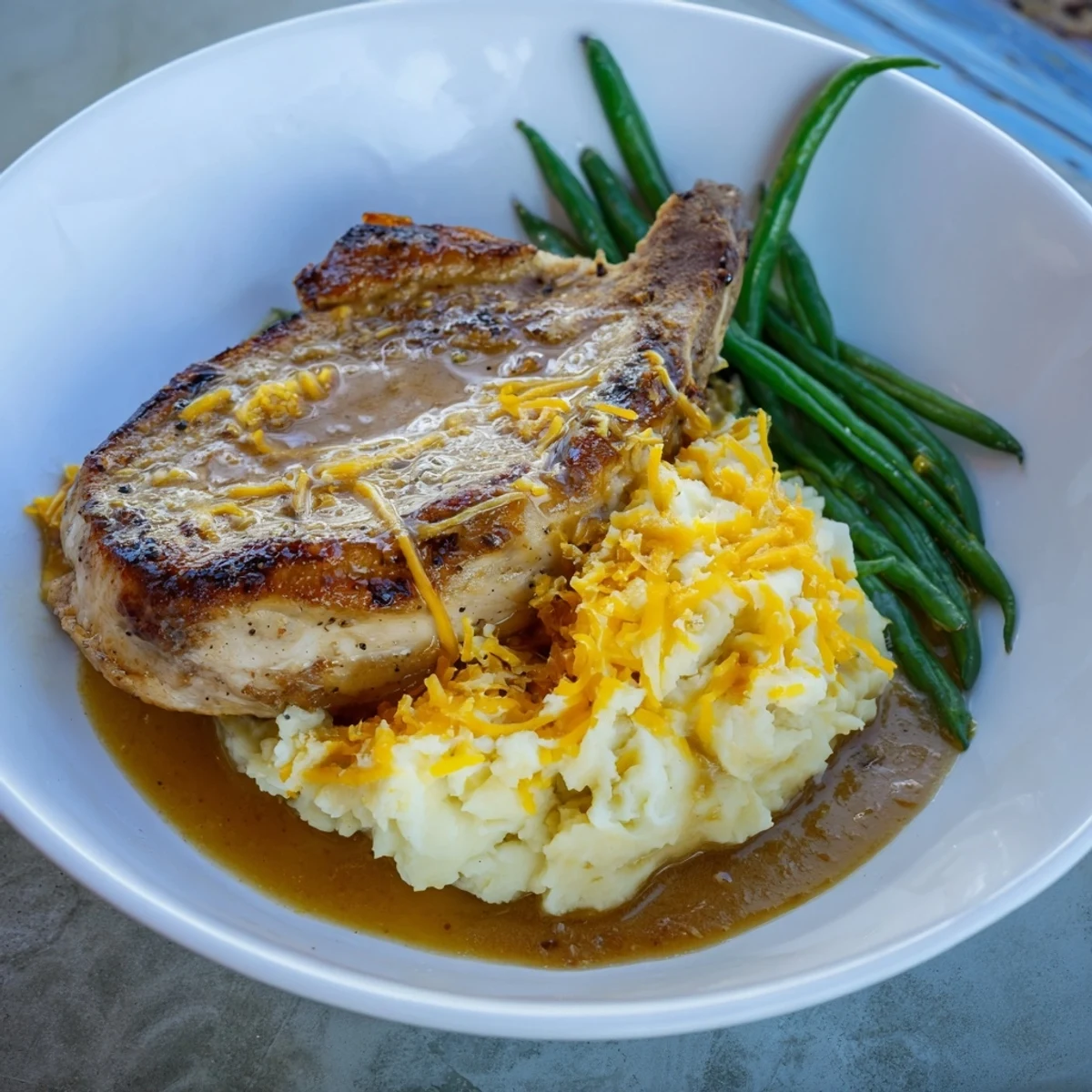 Savory Pork Chops & Cheddar Mash Bowl plated with a silky gravy and fresh green beans.