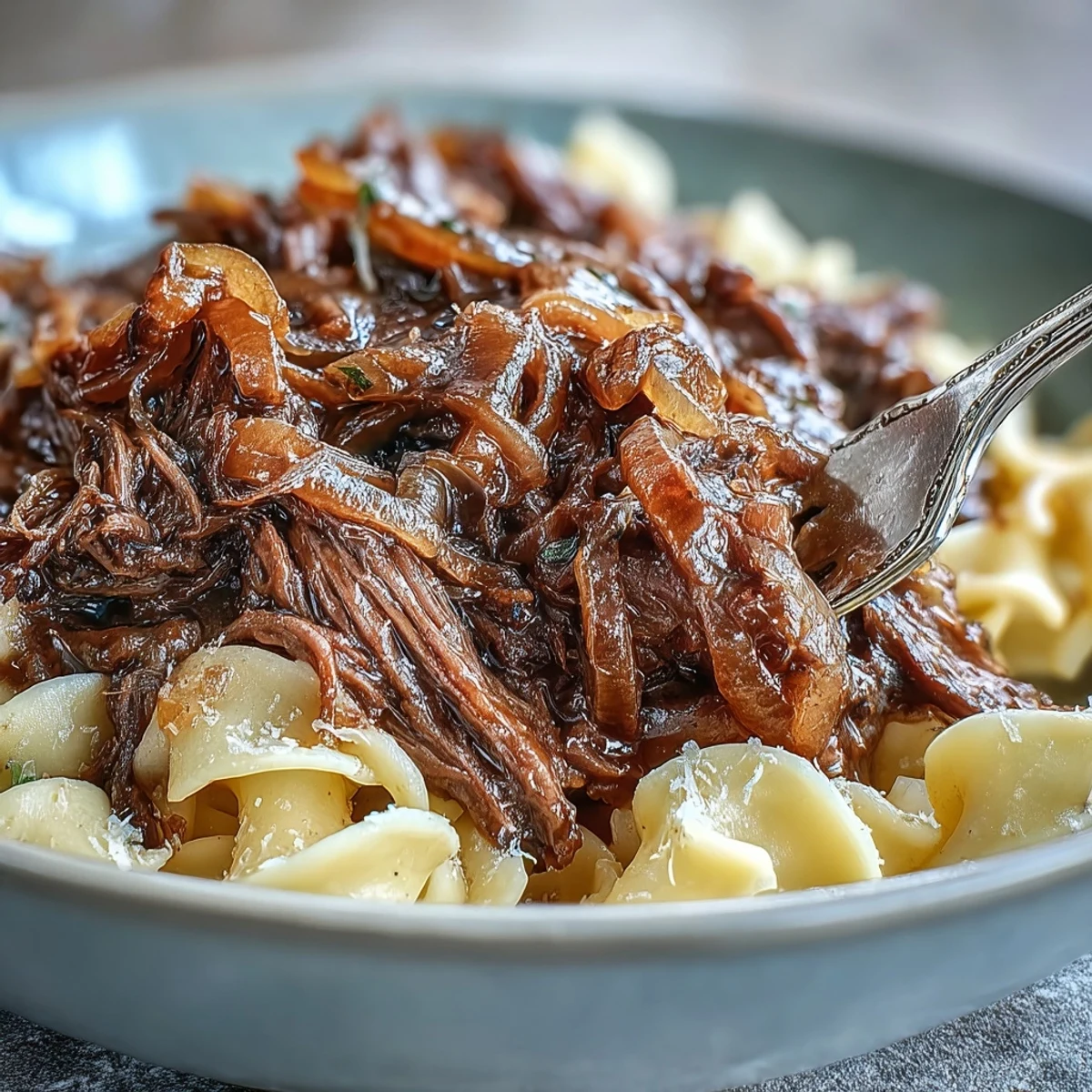 Crockpot French Onion Pot Roast Pasta with tender shredded beef and caramelized onions ladled over buttery egg noodles.
