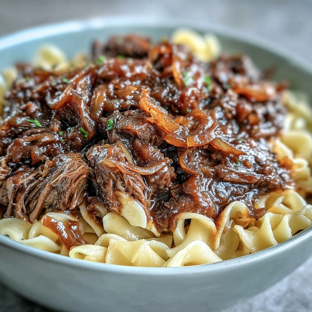 Slow-cooked Crockpot French Onion Pot Roast Pasta topped with melted Gruyère and fresh parsley on a rustic plate.