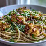 Plated Cauliflower, Anchovy and Raisin Spaghetti topped with fresh parsley and a lemon twist.