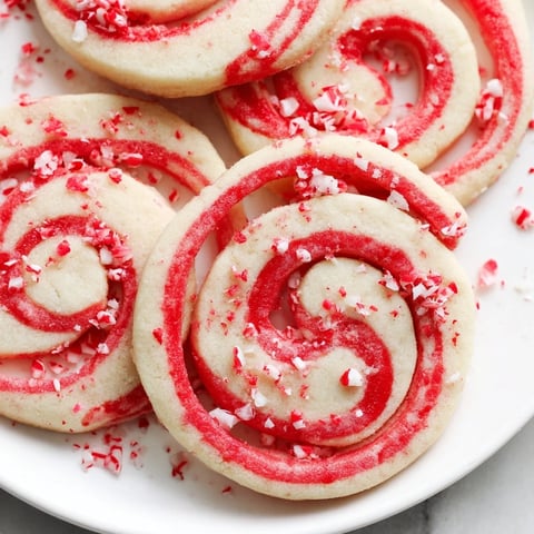 Vibrant red and white Candy Cane Pinwheel Cookies, swirled beautifully and ready to enjoy with a warm drink.