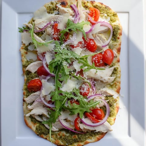 Golden, bubbly Pesto Chicken Flatbread with mozzarella, tomatoes, and red onion, a delightful Italian meal.