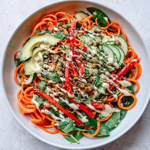 Vibrant Carrot Noodle Skincare Bowl filled with spiralized carrots, crisp veggies, creamy avocado, and drizzled with zesty tahini-lime dressing.