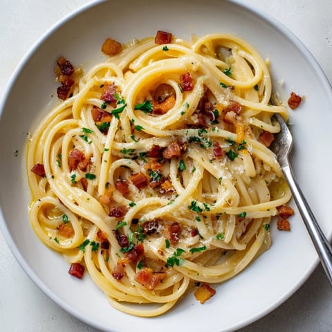 Golden linguine pasta tossed with crispy bacon, garlic, and fresh parsley, served hot in a shallow white bowl.  