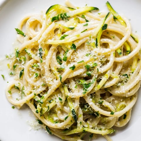 Spiralized zucchini noodles and spaghetti tossed in a zesty lemon butter sauce, garnished with fresh parsley and grated Parmesan, on a white plate.  