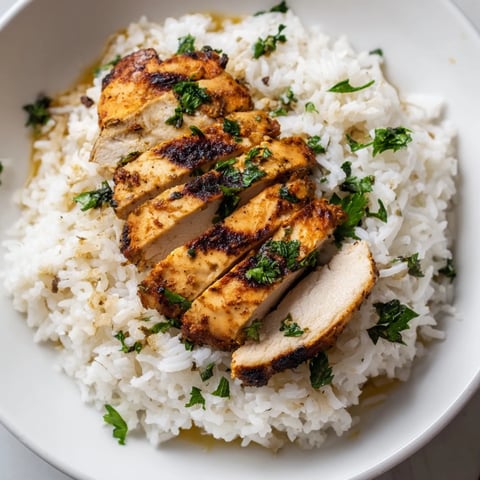 Golden grilled chicken breast slices rest atop fluffy, buttery rice infused with minced garlic and fresh parsley, with a bright lemon wedge on the side.