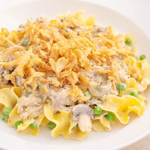 Spoonful of rich creamy Tuna Noodle Casserole with crispy onion topping, full of savory flavors.