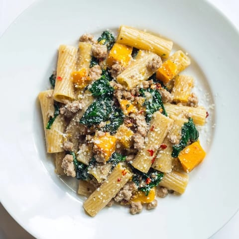 A hearty bowl of creamy rigatoni with butternut squash featuring vibrant sausage pieces and Swiss chard.