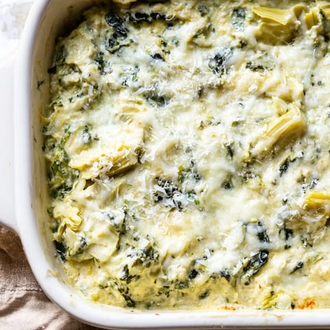 A close-up of creamy, golden Cheesy Spinach Artichoke Dip, bubbling from the oven, so inviting.