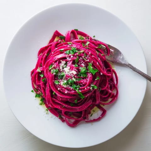 Freshly rolled beet noodle pasta, cut into ribbons and served with a pat of butter and basil on a rustic wooden table.  