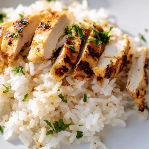 Fork-tender garlic butter rice is served hot, featuring tender grains and a savory aroma, perfectly paired with sliced, juicy grilled chicken and fresh parsley garnish.