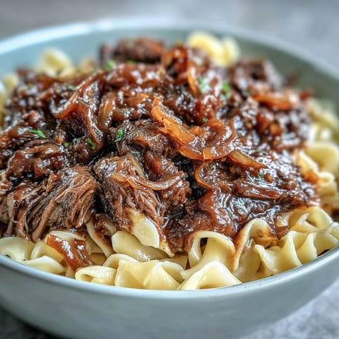 Slow-cooked Crockpot French Onion Pot Roast Pasta topped with melted Gruyère and fresh parsley on a rustic plate.