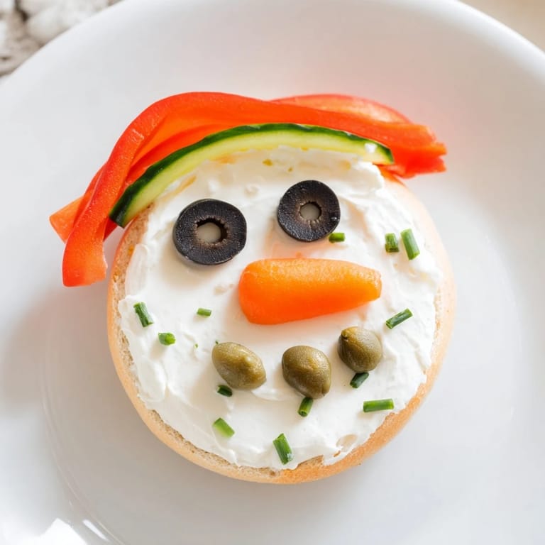 Festive snowman mini bagel sandwiches, decorated with colorful veggies and creamy cream cheese.