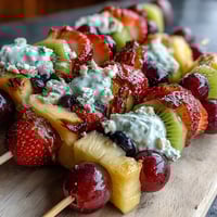 Rainbow fruit kabobs with yogurt dip feature vibrant strawberries, oranges, pineapple, grapes, and blueberries arranged on skewers for a festive snack.